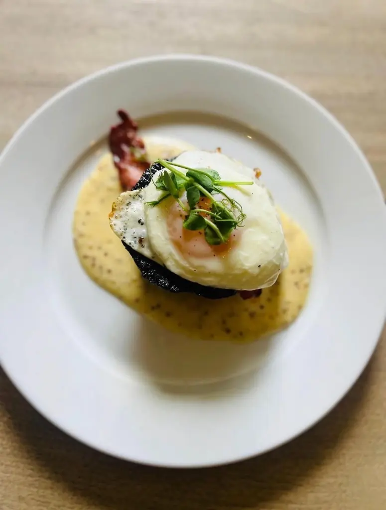 A breakfast plate with an egg, bacon and sauce